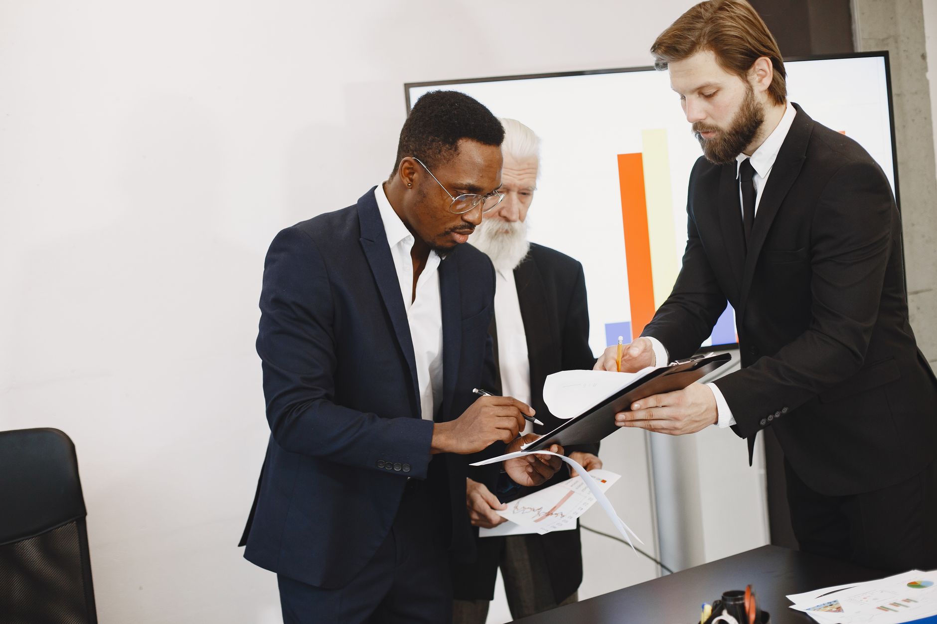 Three businessmen engaged in document signing in a modern office setting. — Medicare Supplement Plans - Plan F Coveri